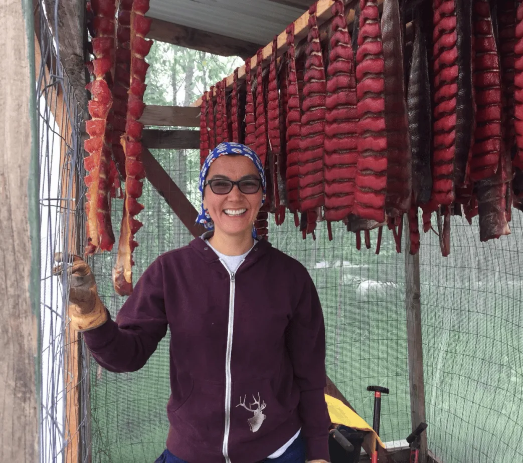 Mary Peltola beside salmon strips hanging to dry in the smokehouse.