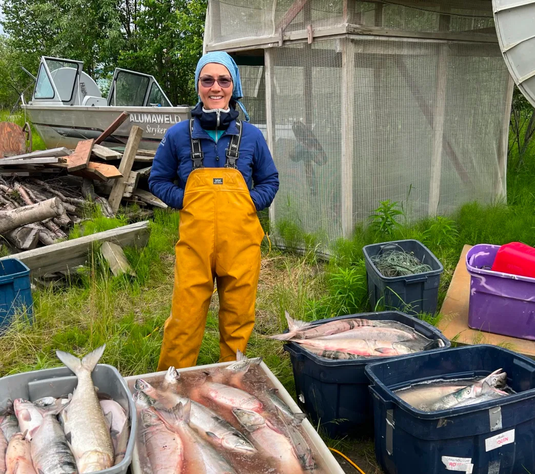 Mary Peltola in rain gear beside totes of fresh salmon.