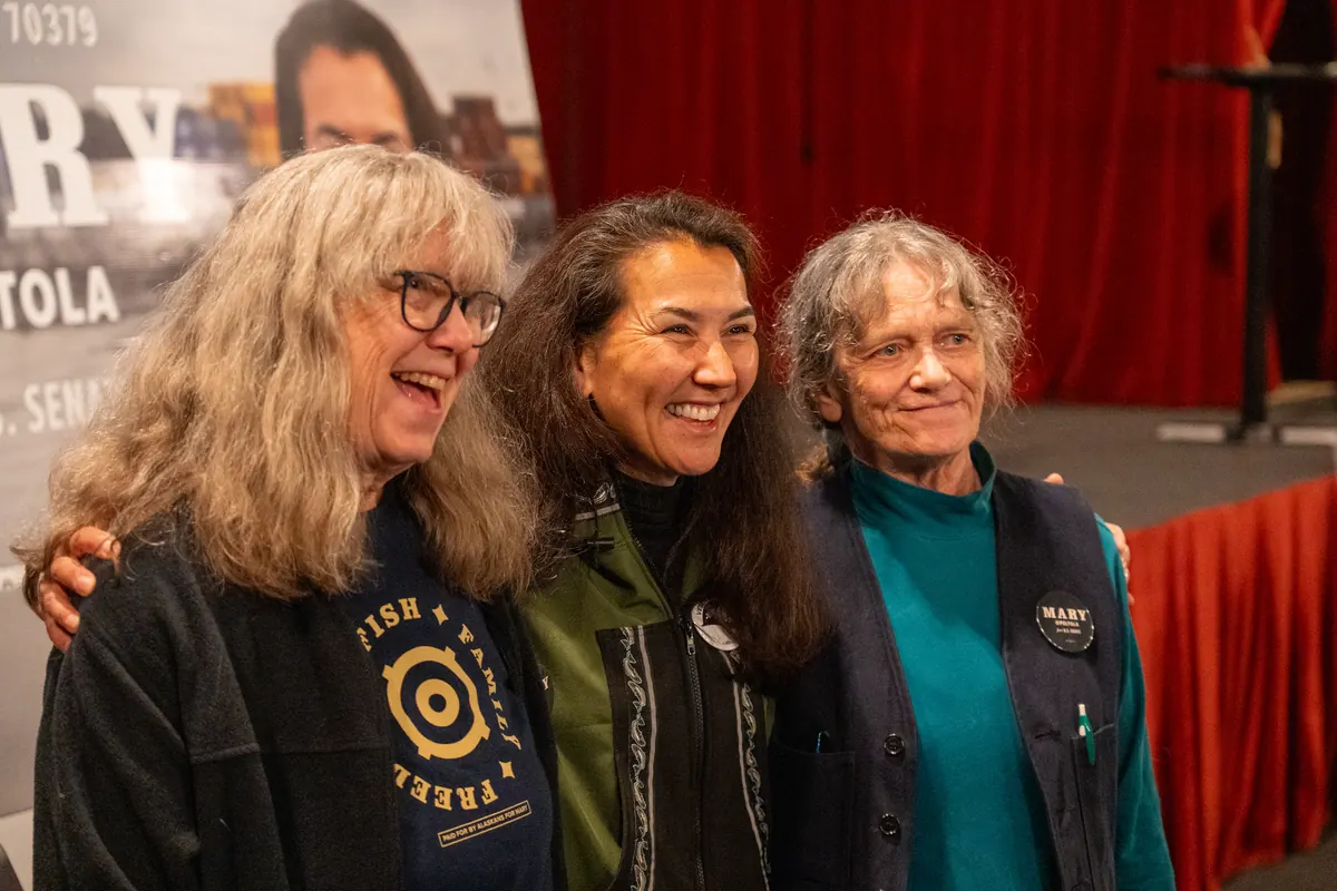 Mary Peltola stands arm in arm with two supporters.