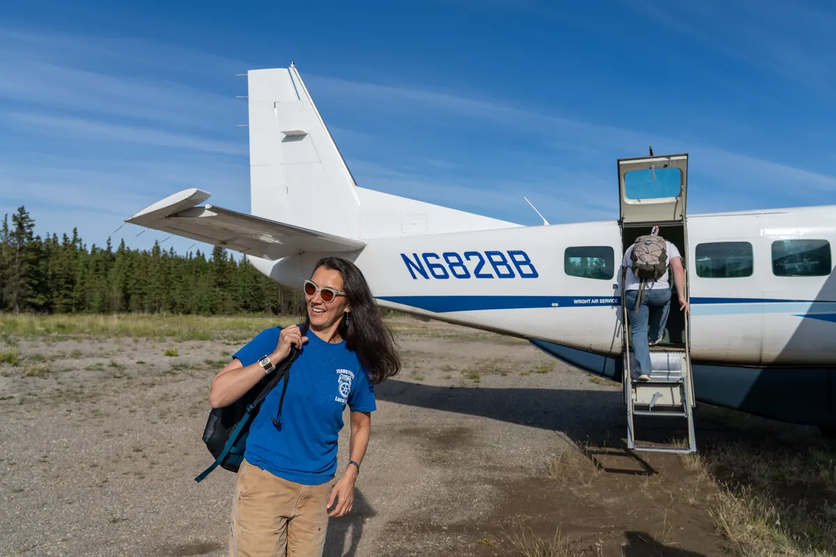Mary Peltola, backpack on her shoulder, beside a bush plane on a gravel airstrip.