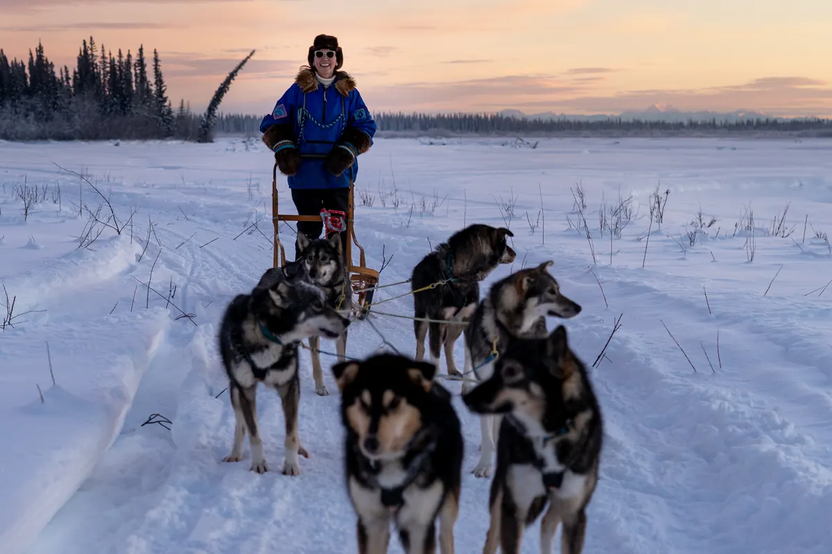 Mary Peltola drives a dog team across the snow at dusk.
