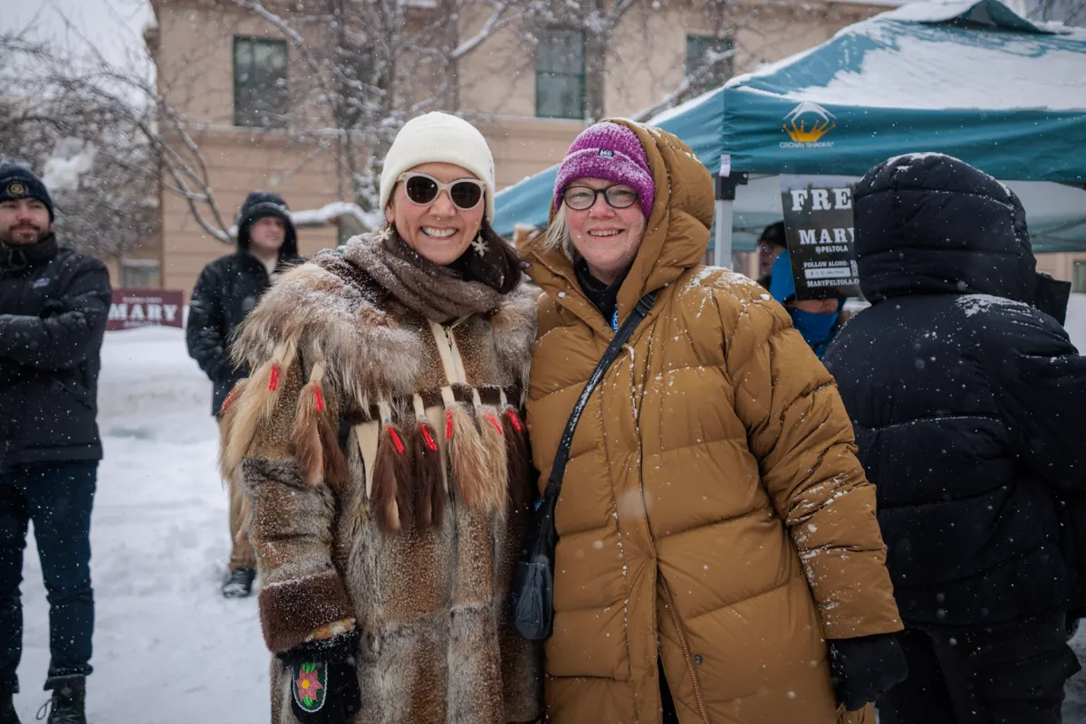 Mary Peltola, in a fur parka, with a supporter on a snowy street.