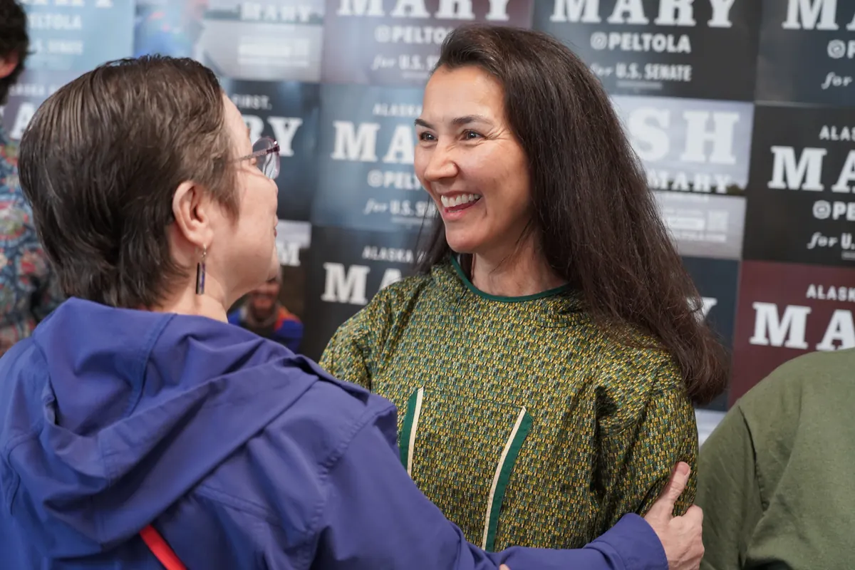 Mary Peltola laughs with a supporter in front of a wall of campaign posters.