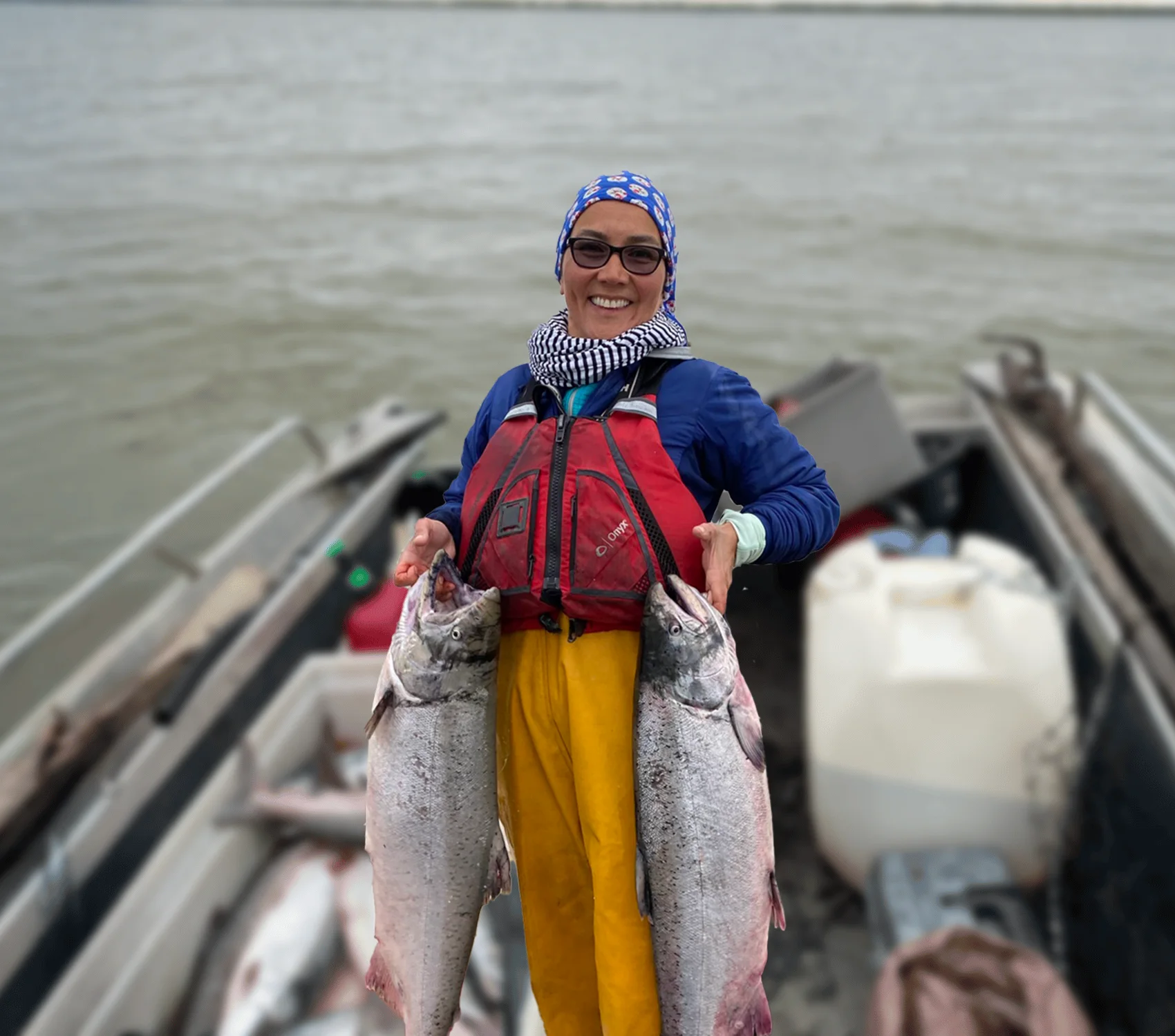 Mary Peltola in a skiff on the river, holding up two salmon.